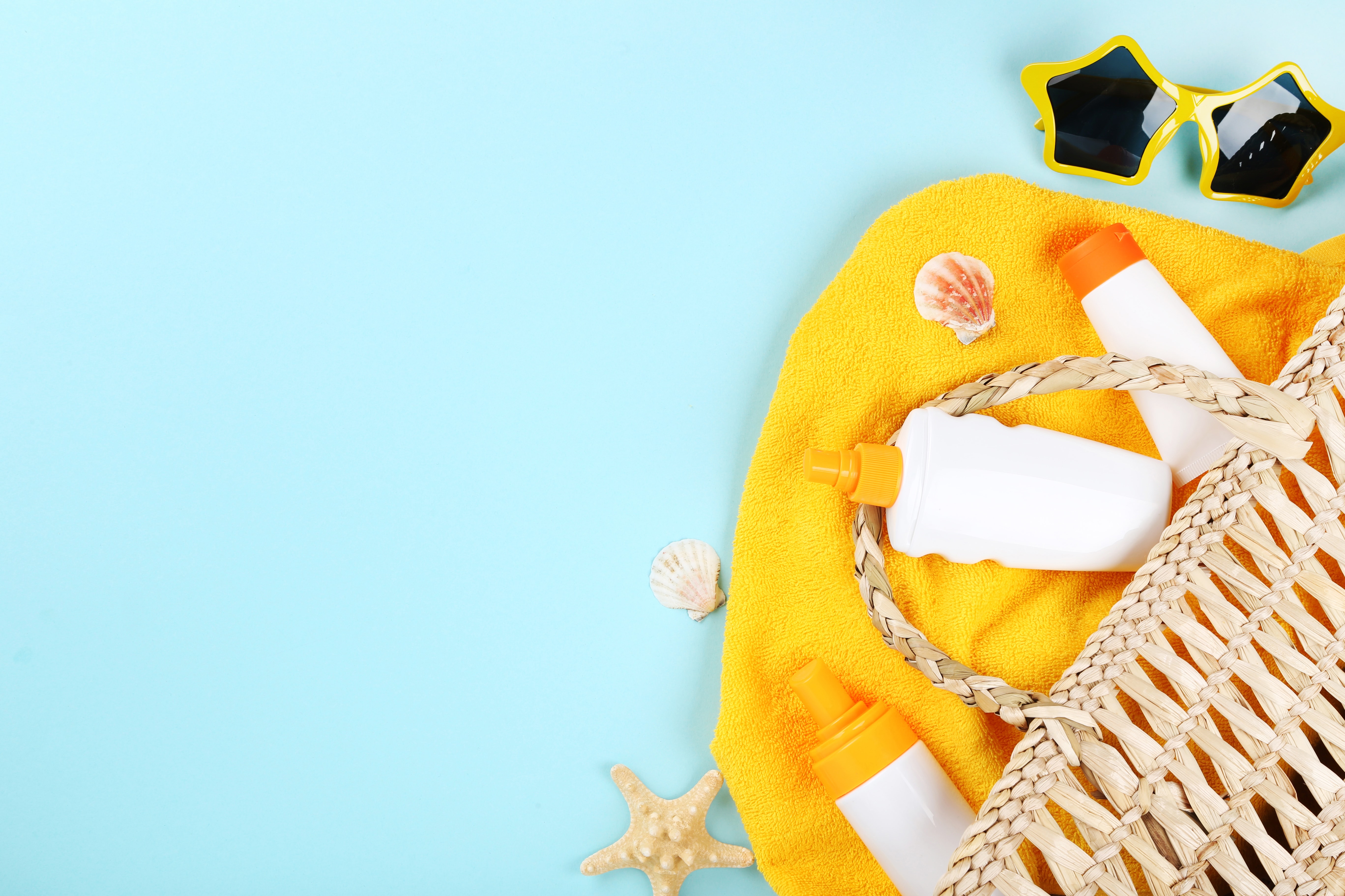 flat lay with beach towel, straw bag, sun cream, sea shells and sunglasses