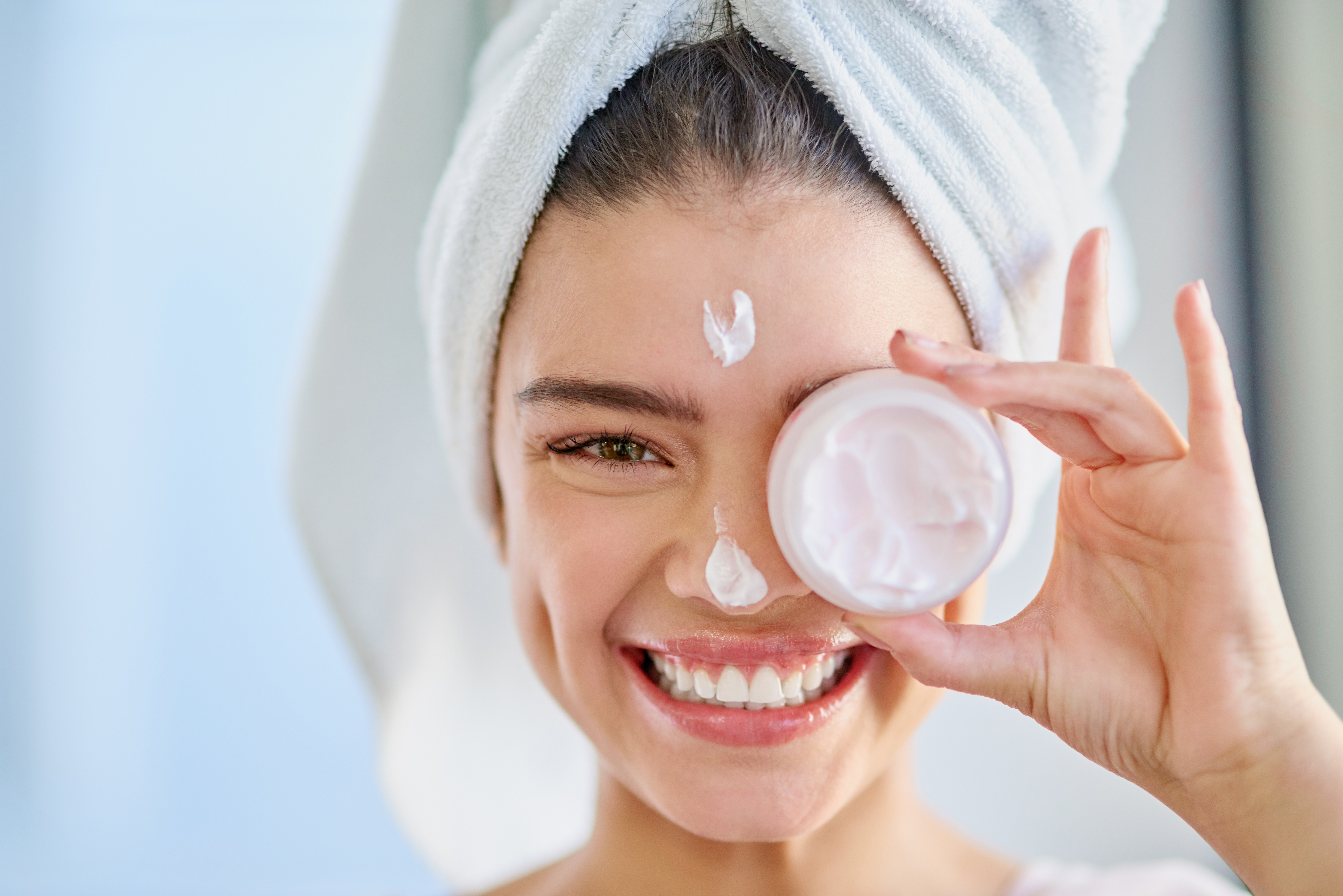 young woman with towel applying face cream, moisturiser, young smiling woman skincare