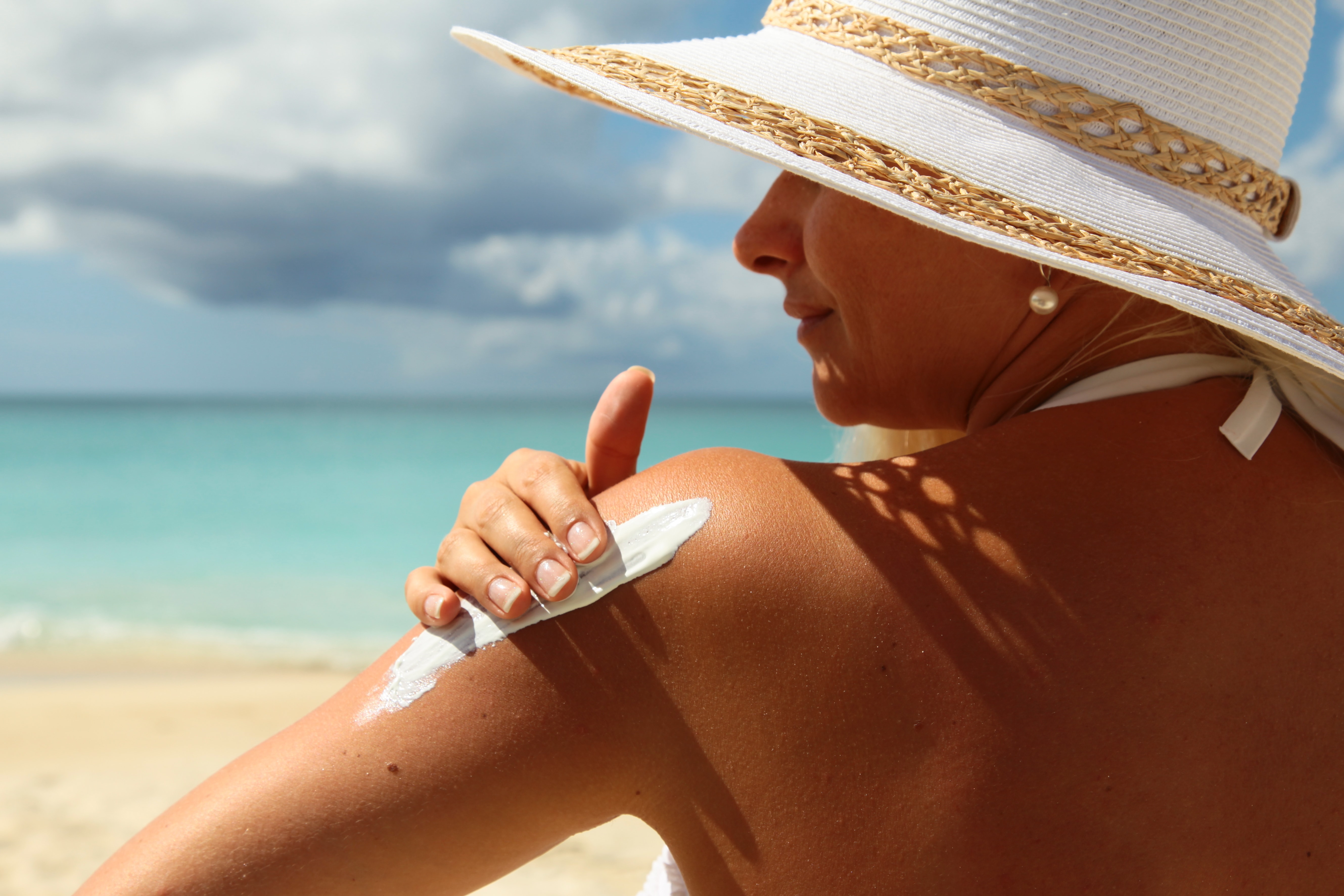 woman applying sun cream on beach wearing sun hat
