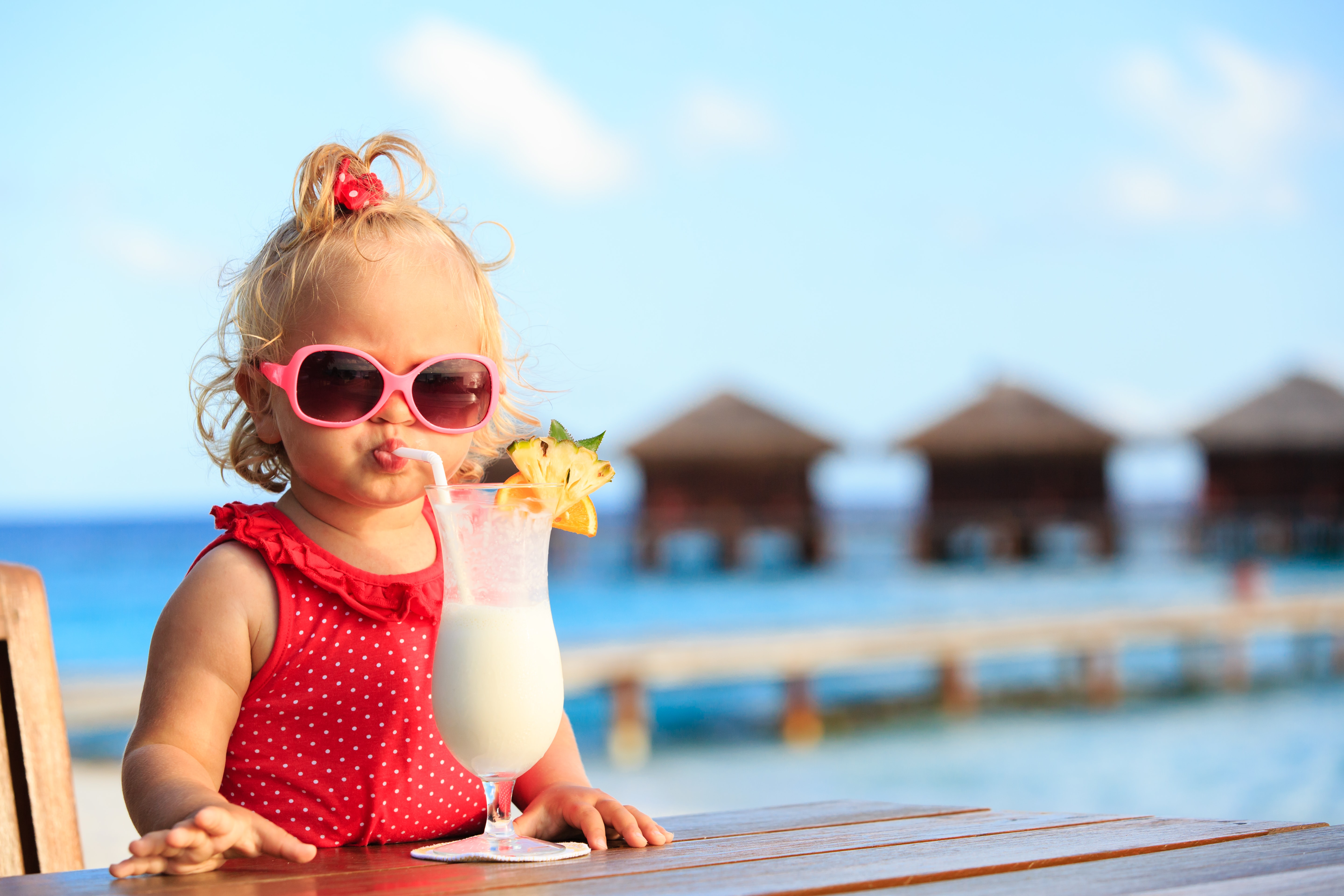 young girl drinking milkshake on holidays, wearing sunglasses and a swimsuit