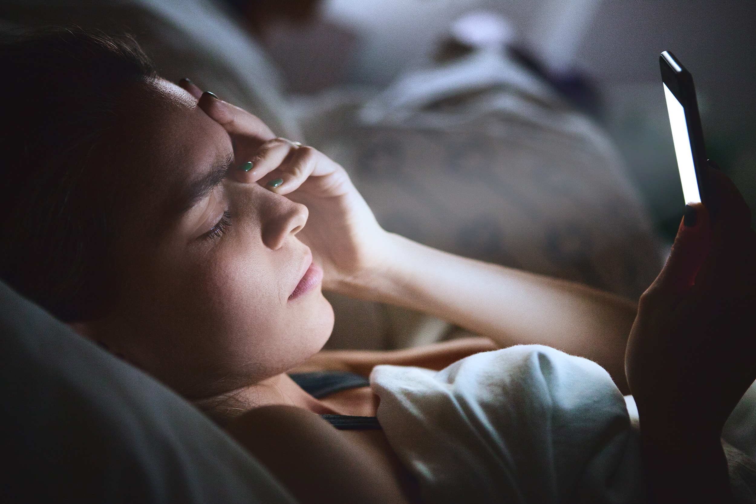 woman in bed looking at her phone unable to sleep