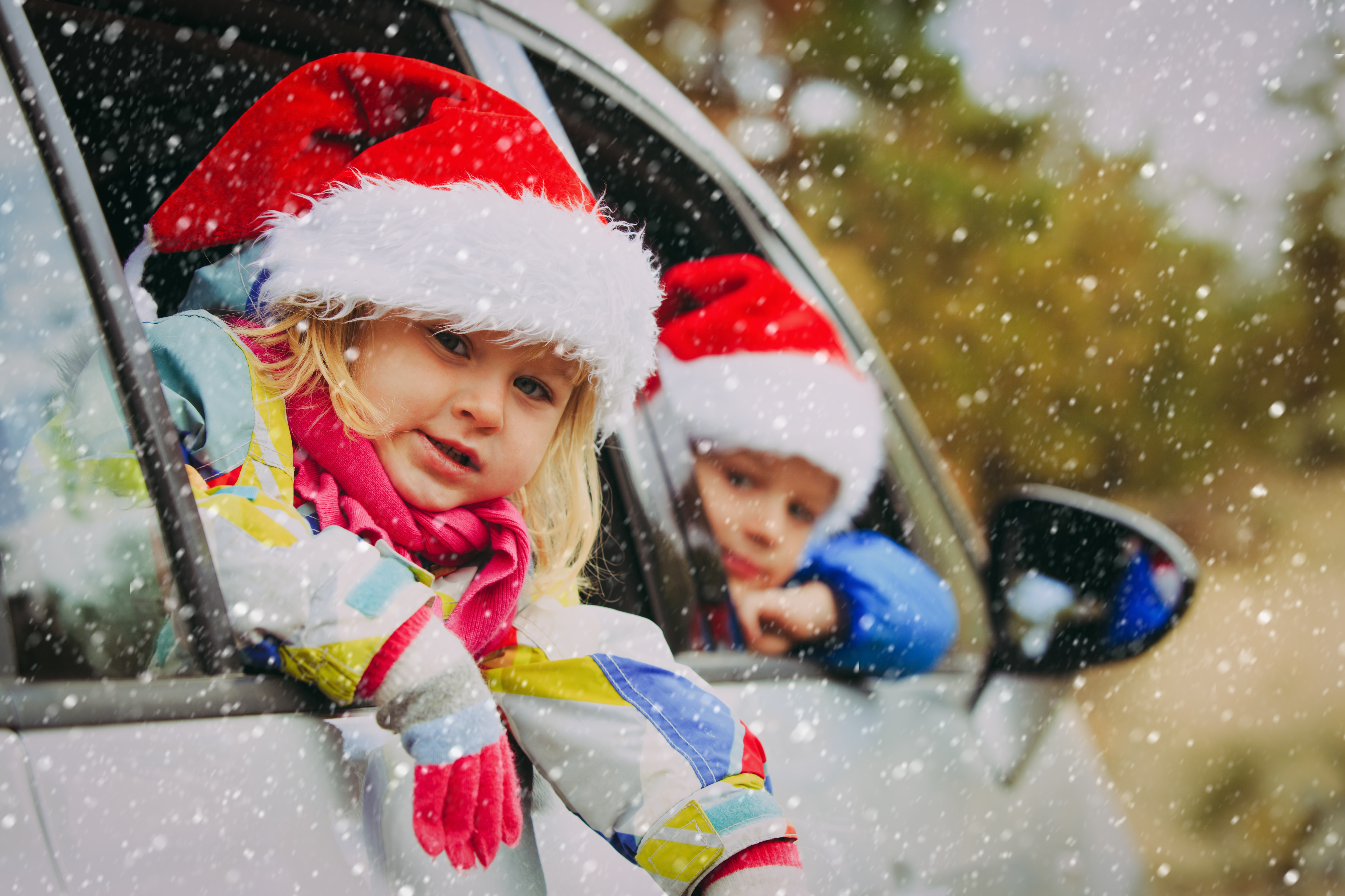 kids at Christmas time, wearing Santa hats leaning out a car window in the snow